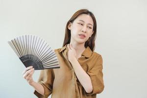 Suffering summer heat stroke, hot weather, tired asian young woman, girl sweaty and thirsty, refreshing with hand in blowing, wave fan to ventilation when temperature high at home, house.on background photo