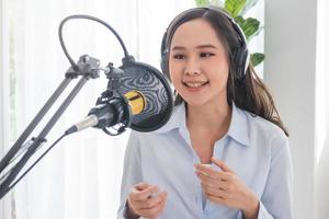 Beautiful asian young woman radio host working, setting microphone, preparing to speak before recording podcast and live on social media. Technology of on-air online in broadcasting at home studio.