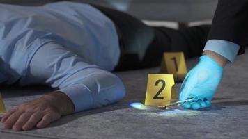forense especialista examinando Concha invólucro com pinças às crime cena investigação. polícia usando uma ampliação vidro para examinar a tripas do a bala este morto a cadáver. video