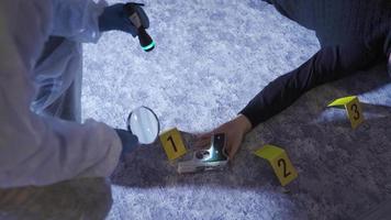 Forensic expert examining the body of the man who committed suicide. The forensic scientist examining the body examines the evidence and the gun with a magnifying glass.