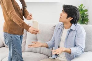 infidelidad, sospecha asiático joven Pareja amor lucha relación, esposa participación Teléfono móvil, teléfono inteligente engañando en teléfono, regaño marido acerca de desconfianza, desconfianza y celos cuando sentado a hogar. foto