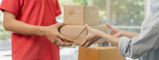 Delivery, asian young man, male postman holding cardboard box parcel, carton or mail in red uniform send to client, customer woman received from messenger, Service business, shopping online. photo