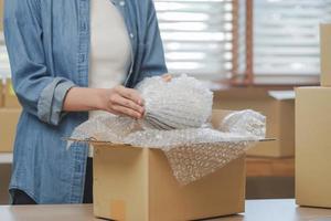 Small business entrepreneur SME, hand of woman owner packing product, checking parcel before into cardboard box after receive order from customer, working at home office. Merchant online, ecommerce. photo