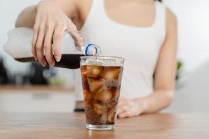 sediento, asiático joven mujer, niña tenencia, torrencial frío reajuste salarial suave bebida soda, espumoso agua con hielo dulce azúcar desde botella dentro vaso en su mano. salud cuidado, sano dieta estilo de vida concepto. foto