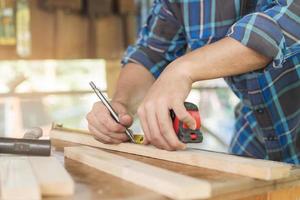 Carpentry professional, hand of asian young man, male carpenter use tape measure, tool on board wood in small shop. Woodwork, furniture making, construction industry. Owner small business people. photo