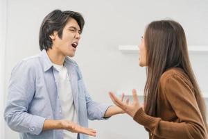 asiático joven Pareja lucha en pie en blanco fondo, relación en problema. diferente enojado, utilizar emoción gritos a cada otro. discutir marido tiene expresión de decepción y trastornado con esposa. foto