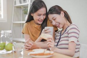 Happy lesbian, pleasure asian young two women, girl gay or close friend, couple love , moment spending good time together, having date eating breakfast on table at home. Activity of leisure, relax. photo