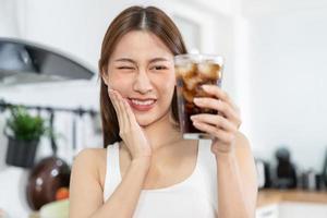 Health asian young woman touching cheek, expression, suffering from toothache, decay or sensitivity cavity molar tooth, teeth or inflammation drink cold, sparkling water at home.Sensitive teeth people photo