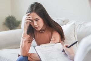 Psychology, depression. Sad, suffering asian young woman consulting with psychologist, psychiatrist while patient counseling mental with doctor woman taking notes at clinic. Encouraging, therapy. photo