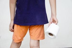 Closeup boy holds roll of tissue paper, need to go to the toilet. Concept, health problem, diarrhoea, hemorrhoids, use tissue paper for hygienic and sanitary.  Health care in daily life. photo