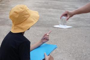 estudiante chico usa sombrero, sostener libro, aprendizaje Ciencias experimentar acerca de aire presión desde vaso de agua cuales cubierto por papel. concepto, Ciencias tema actividad, educación. aprendizaje por haciendo foto