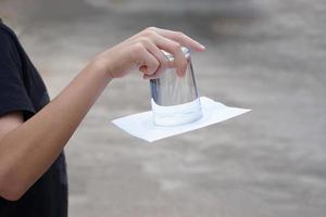 de cerca mano sostener y giro un vaso de agua terminado abajo. cubierto el vaso con papel. concepto, Ciencias experimentar acerca de aire y líquido presión. fácil Ciencias tema actividad, educación. foto