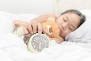 hand girl reaching to turn off alarm clock on bed photo