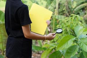 Closeup boy is learning about botanical plants lesson, holds magnifying glass and book. Concept, Science and environment project assignment from school. Self learning outside. photo