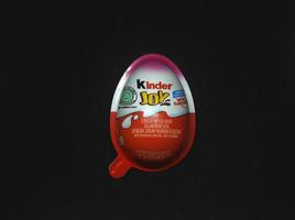 Jakarta, Indonesia - March 19th, 2023 - Kinder Joy egg chocolate milk sweet sugary snack with surprise toy inside isolated children food photo on dark black background.