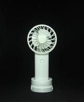 Small useful hand or desk white fan photo isolated on dark black background. Simple technology for cooling breezing air at the office or home.