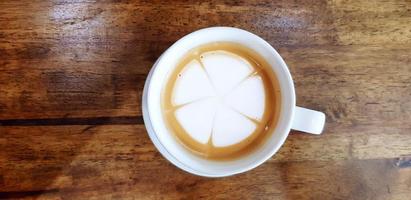 Top view of white cup of hot latte art in flower or leaves drawing  on dark brown wooden background or table with copy space. Refreshment drinking and Food design. photo