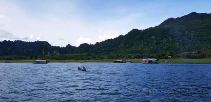 Long tail boat on river with many home or resort, green mountain, Blue sky and clouds at Srinakarin lake Kanchanaburi, Thailand. Beautiful landscape view of Natural, Nature wallpaper and Life on wate photo