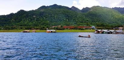 largo cola barco en río con muchos hogar o complejo, verde montaña, azul cielo y nubes a srinakarin lago kanchanaburi, tailandia hermosa paisaje ver de natural, naturaleza fondo de pantalla y vida en agua foto
