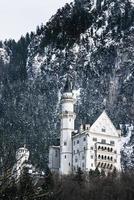 Beautiful view of the Neuschwanstein Castle or Schloss Neuschwanstein  on a winter day, with the mountains and trees capped with snow all around it. photo