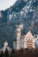 Beautiful view of the Neuschwanstein Castle or Schloss Neuschwanstein  on a winter day, with the mountains and trees capped with snow all around it. photo