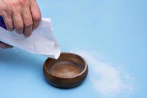 hand of an elderly man is about to pour something into a bowl from a paper bag on a blue background photo