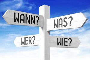 When, What, Who, How Questions in German - Wooden Signpost with Four Arrows and Sky in Background photo