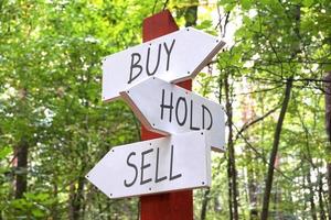 Buy, Hold, Sell - Wooden Signpost with Three Arrows, Forest in Background photo