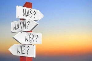 What, When, Who, How - Wooden Signpost with Four Arrows in German photo