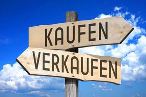 Buy, Sell in German - Wooden Signpost with Two Arrows, Sky with Clouds in Background photo