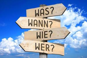 What, When, How, Who Questions in German - Wooden Signpost with Four Arrows photo