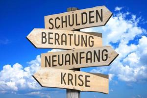 deuda, ayuda, nuevo comienzo, crisis en alemán - de madera señalizar con cuatro flechas