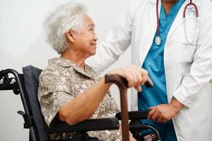 Doctor help Asian elderly disability woman patient holding walking stick in wrinkled hand at hospital. photo