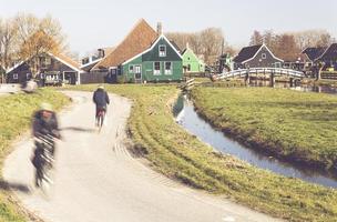 Residents and visitors riding past an old Amsterdam mill in the Zaanse Schans neighborhood photo