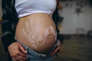 mujer embarazada barriga con niño huellas dactilares en camisa y azul pantalones foto