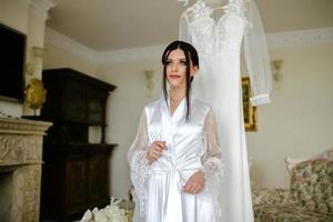 Romantic atmosphere of the bride's morning. Bride in a home. Bride morning preparation. Bride in beautiful dress near the mannequin with dress indoors at home. Enjoy every moment. photo