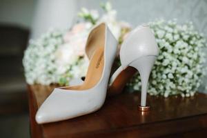 female feet in white wedding sandals with a bouquet of camomiles photo