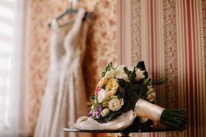 novia con un vestido blanco sosteniendo un ramo de flores moradas y vegetación en el fondo de la hierba verde foto