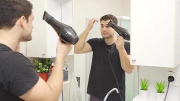 el hombre el secado su pelo con un soplar secadora. en el baño, el joven hombre unidades su mojado pelo con un soplar secadora y estilos él. video