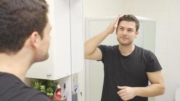 giovane bello uomo guardare a lui stesso nel il specchio. il uomo chi si raddrizza il suo capelli nel il specchio trova lui stesso bello e contento. video