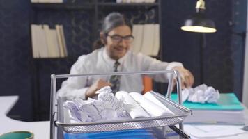 Lazy office worker sitting at desk and busy with other things instead of working. The office worker plays basketball by making balls from papers instead of working. video