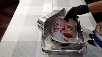 An aged woman cleans the table after eating. Black-gloved hands stack the boxes left over from the delivered lunch. The wrappers are placed in separate waste bins for recycling. video