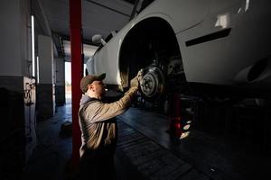 Mechanic in service repair station working with muscle car in lift at sunset shadows. photo