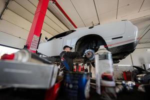 mecánico en la estación de reparación de servicio que trabaja con muscle car, desmantela una rueda en el ascensor. foto