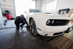 mecánico en la estación de reparación de servicio que trabaja con muscle car. hombre trabajador levanta el coche para diagnosticar el chasis. foto