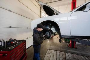 Mechanic in service repair station working with muscle car, dismantles a wheel on lift. photo