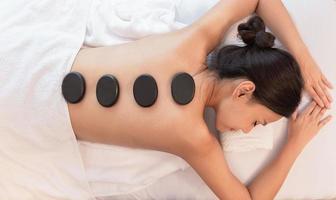 Beautiful young woman relaxing in spa salon with hot stone massage on body. Beauty treatment therapy photo