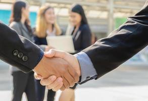 Two business men shaking hands in front of theirs business team standing outdoors photo