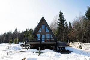 Wooden triangle country tiny cabin house with hot tub spa and suv car with roof rack in mountains. Soul weekends. photo