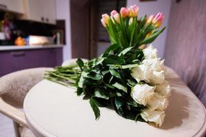 White roses flowers bouquet on wooden table against tulips. photo